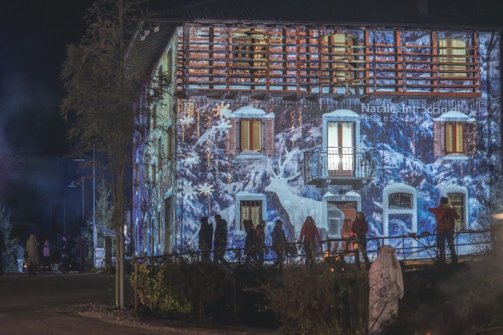 Facciata di una casa del Garda Trentino illuminata da proiezioni natalizie con visitatori a passeggio